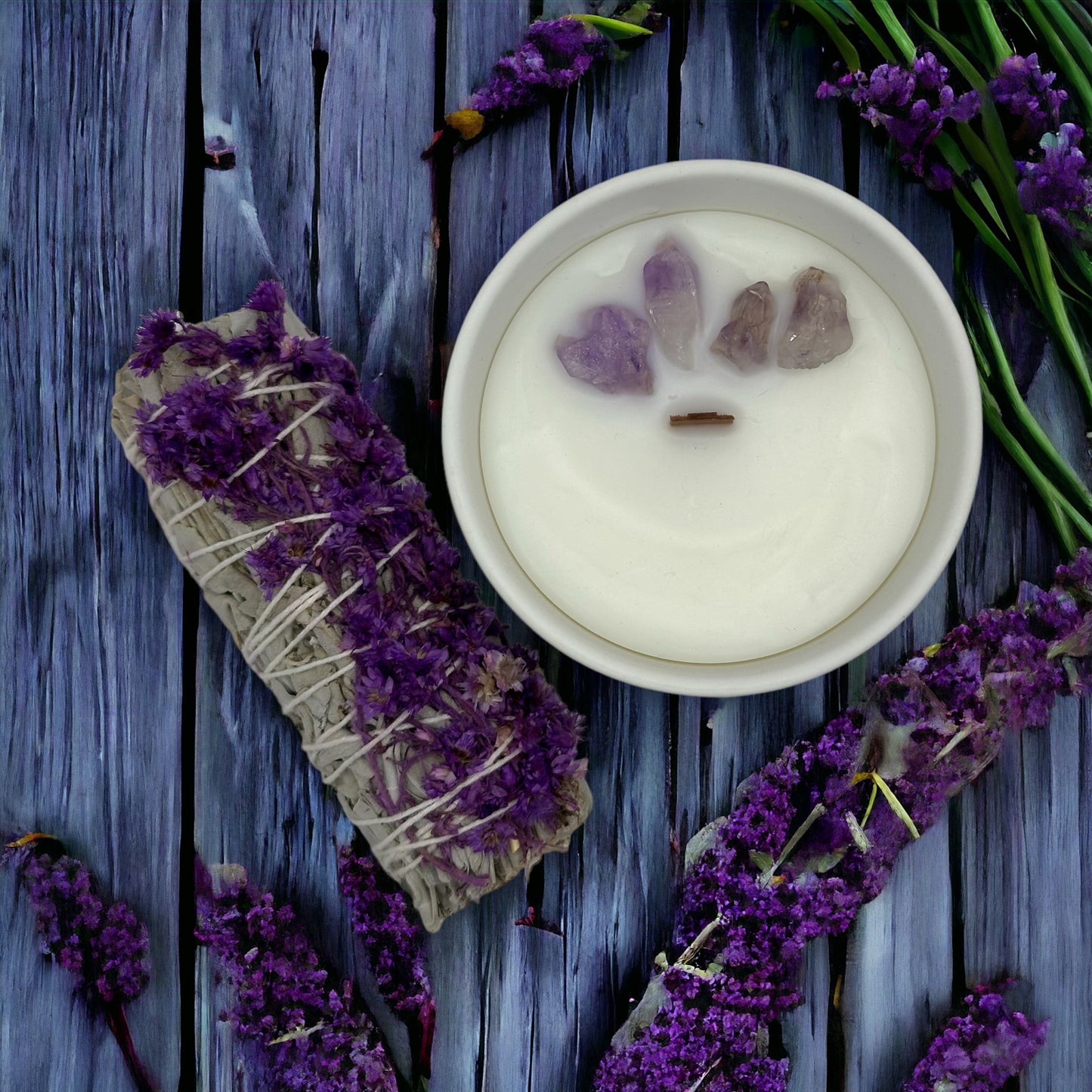 4 oz Lavender Fields candle with wooden wick and amethyst crystals on top, accompanied by a sage bundle with flowers on the side, set against a blueish wooden background for a calming, aromatic ambiance