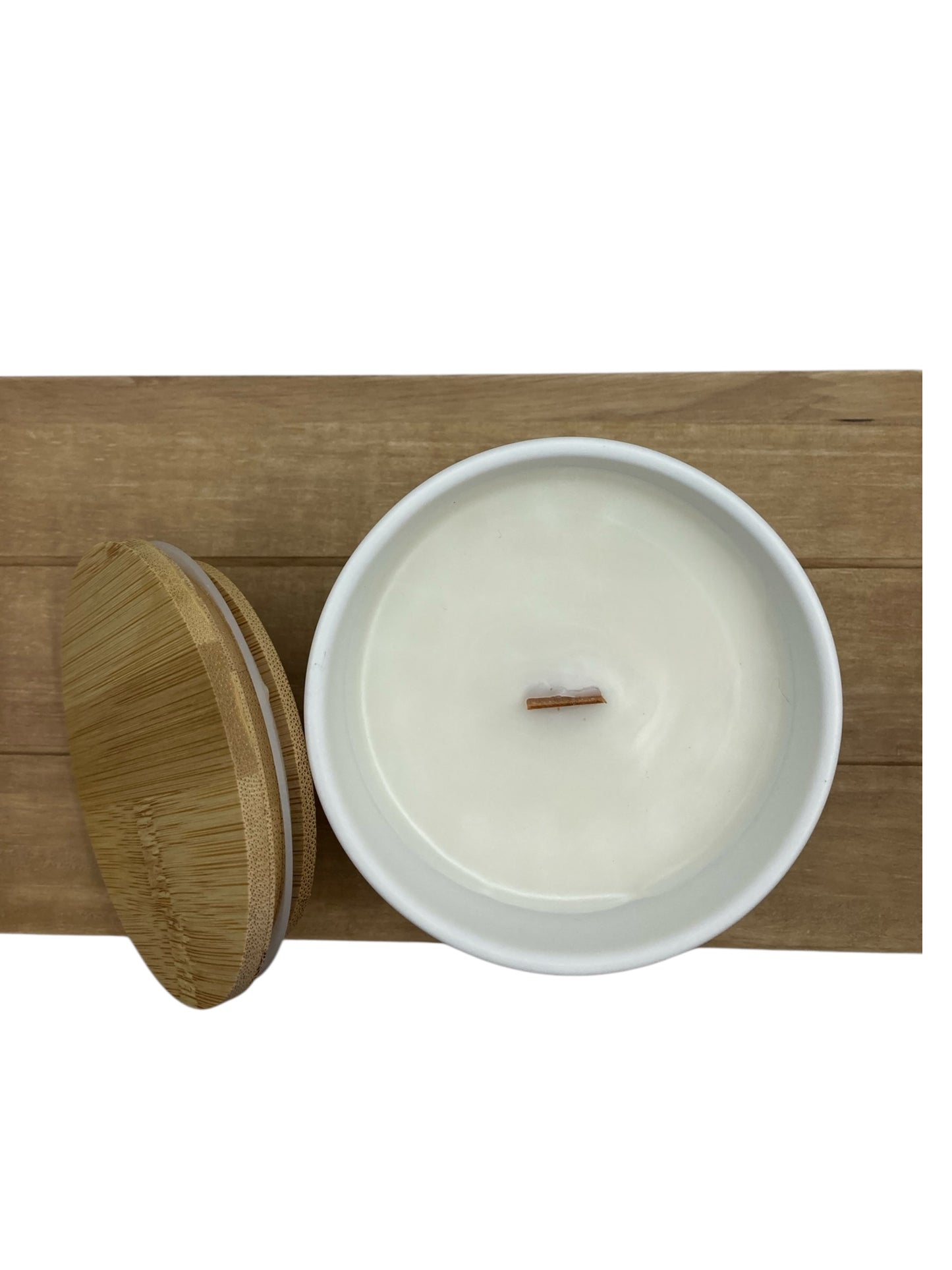 Top-down view of a Renewal candle with a wooden wick, next to a bamboo lid on a wooden tray.