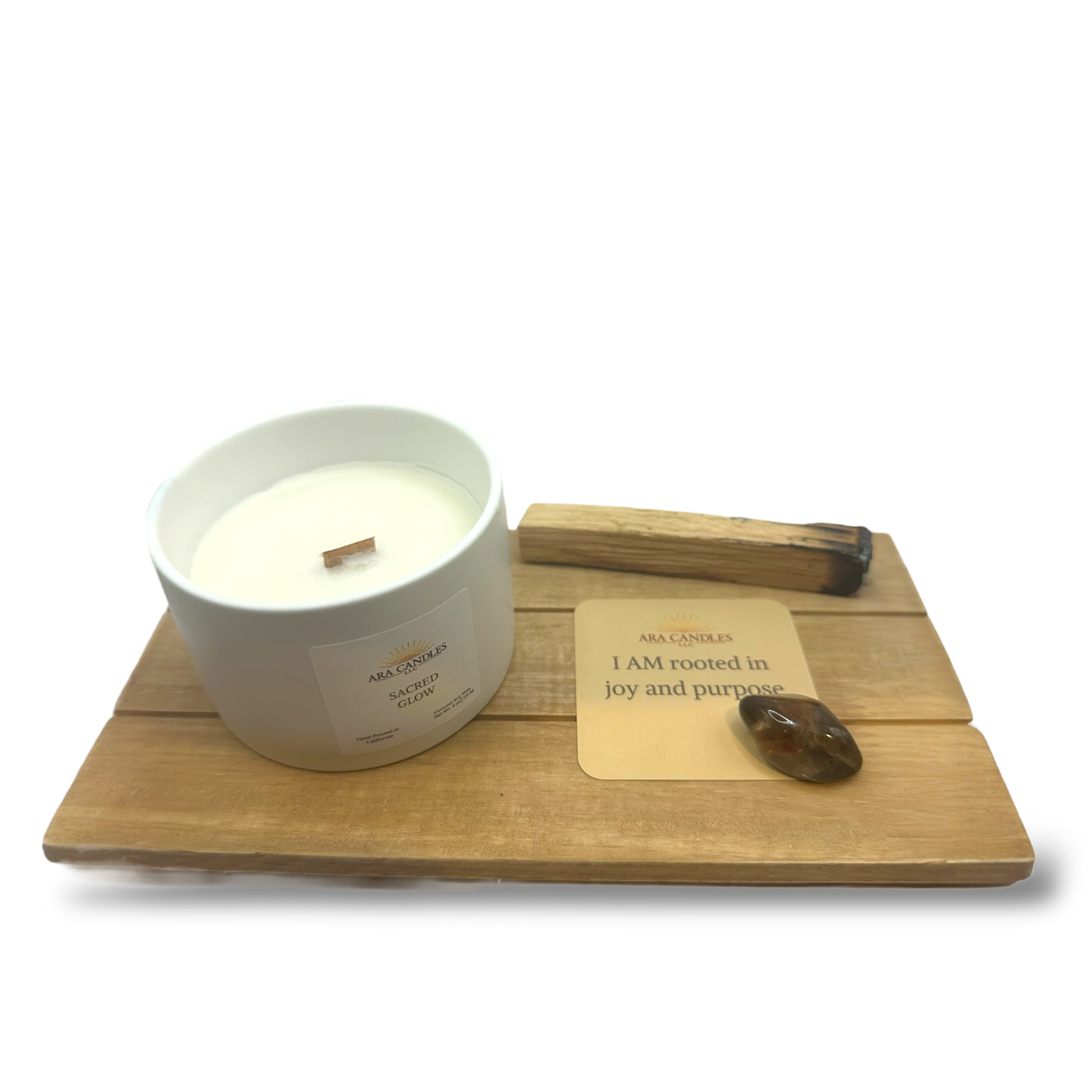 Sacred Glow candle displayed with affirmation card, grounding crystal, and palo santo bundle on wooden tray for energy-clearing rituals.