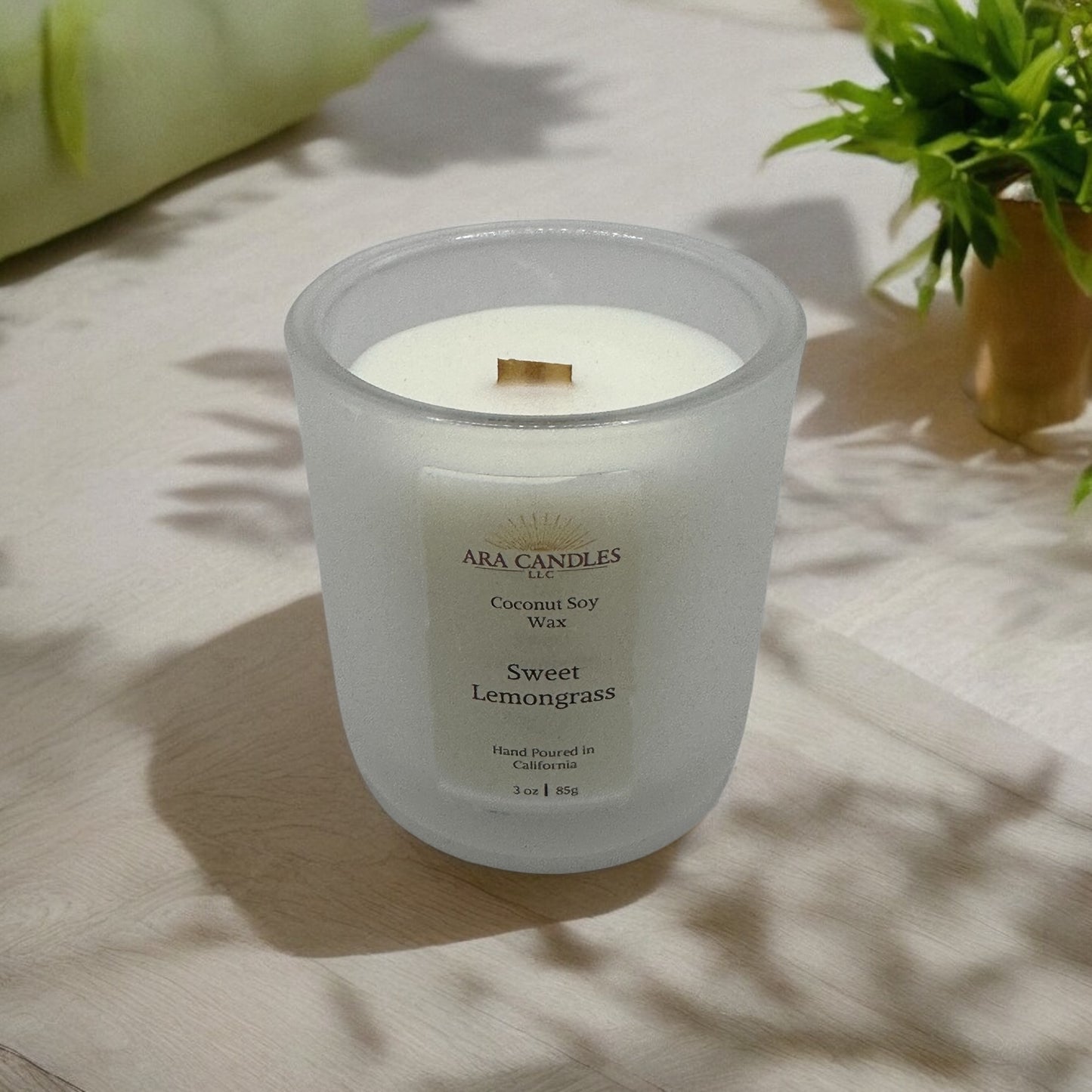 Ara Candles Sweet Lemongrass coconut soy wax candle with wooden wick, hand-poured in California, displayed on a natural wood surface with plant shadows.