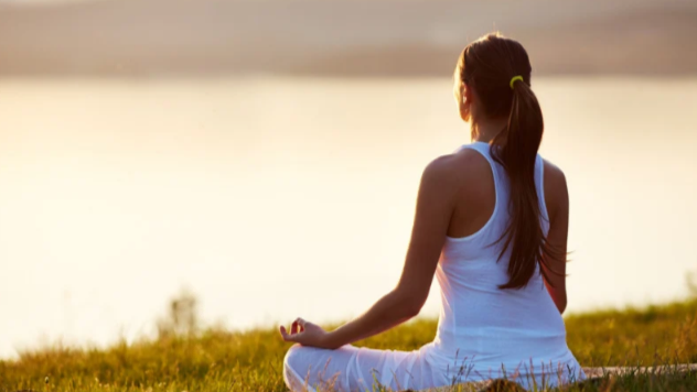 Woman meditating outdoors at sunset, practicing mindfulness and self-care in a peaceful natural setting.