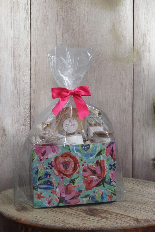 Mother’s Day gift box with floral packaging, pink ribbon, scented candles, diffusers, bath soak, and matches arranged on soft neutral fabric
