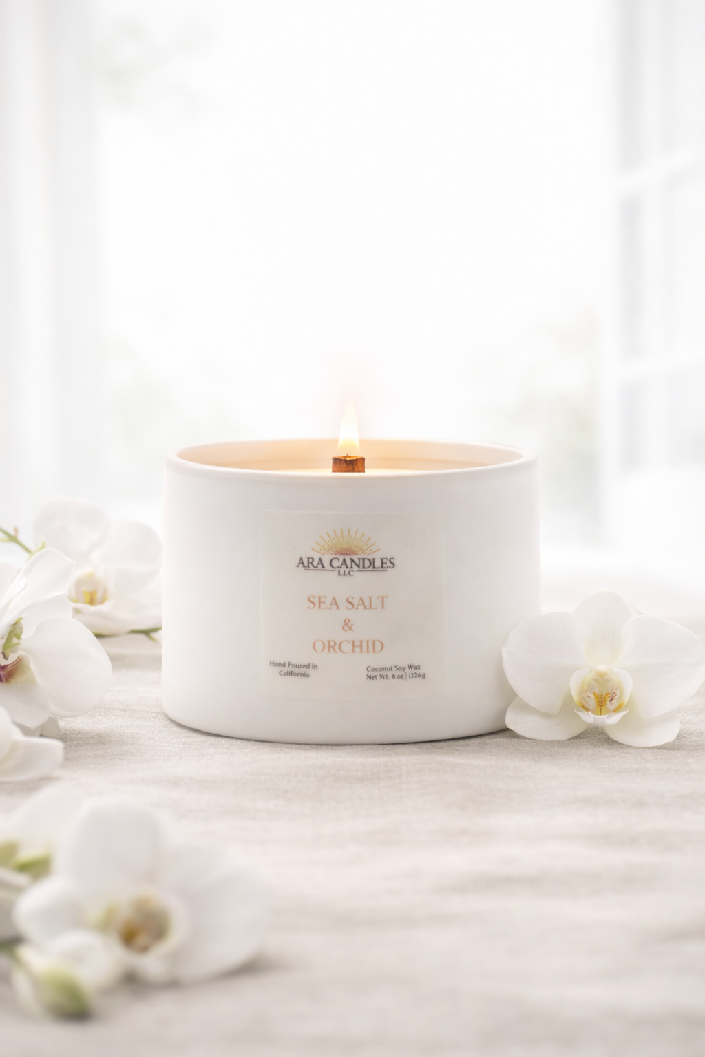 Ara Candles Sea Salt & Orchid candle on a white surface with flowers.