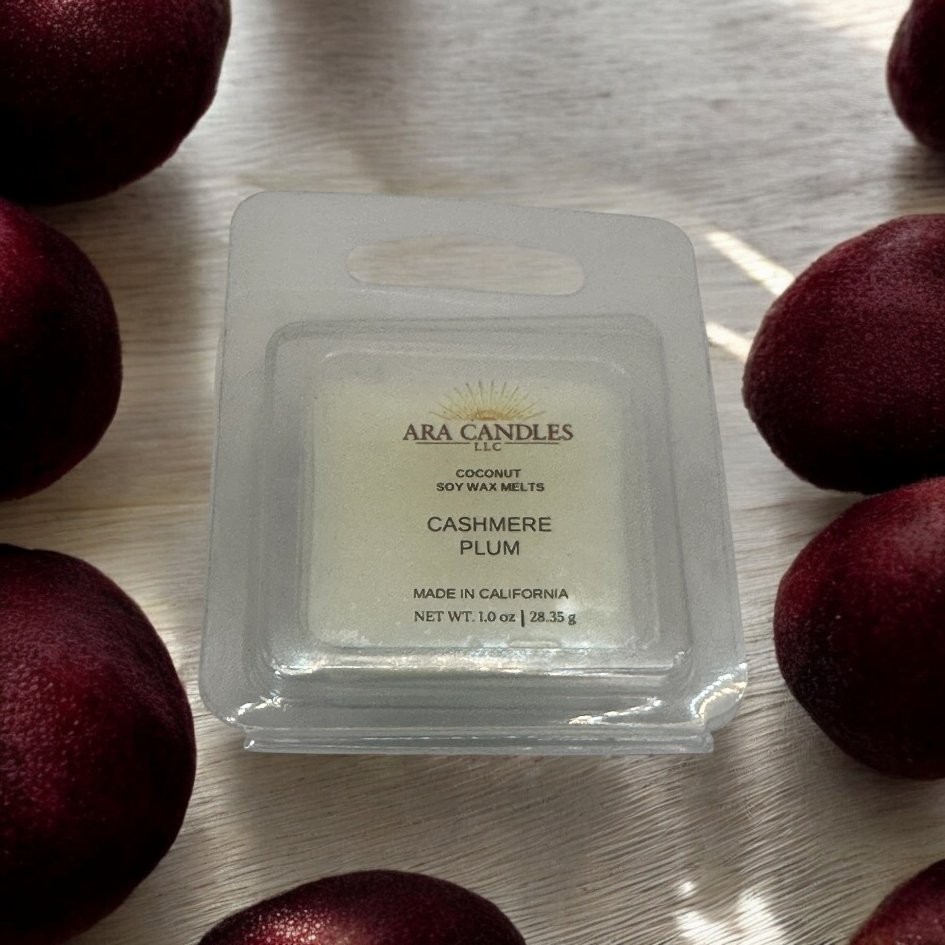 Cashmere Plum 1 oz wax melt with a rich, cozy fragrance, set against a backdrop of plums, offering a warm and luxurious scent in a small, elegant form