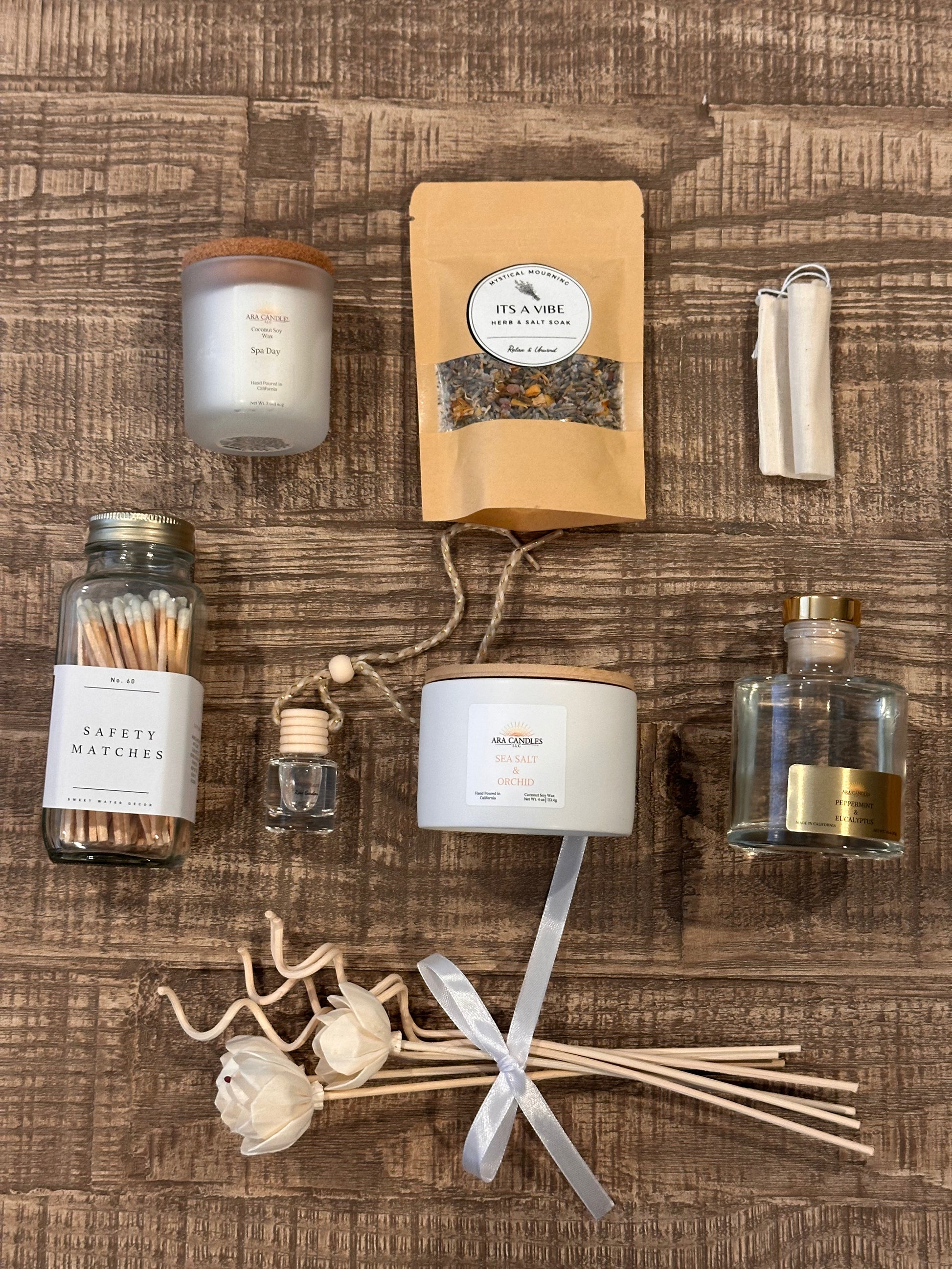Wellness basket featuring Spa Day scented candle, Sea Salt & Orchid candle, Peppermint & Eucalyptus reed diffuser, car diffuser, herbs, and salt bath blends, and matches for a complete relaxation experience